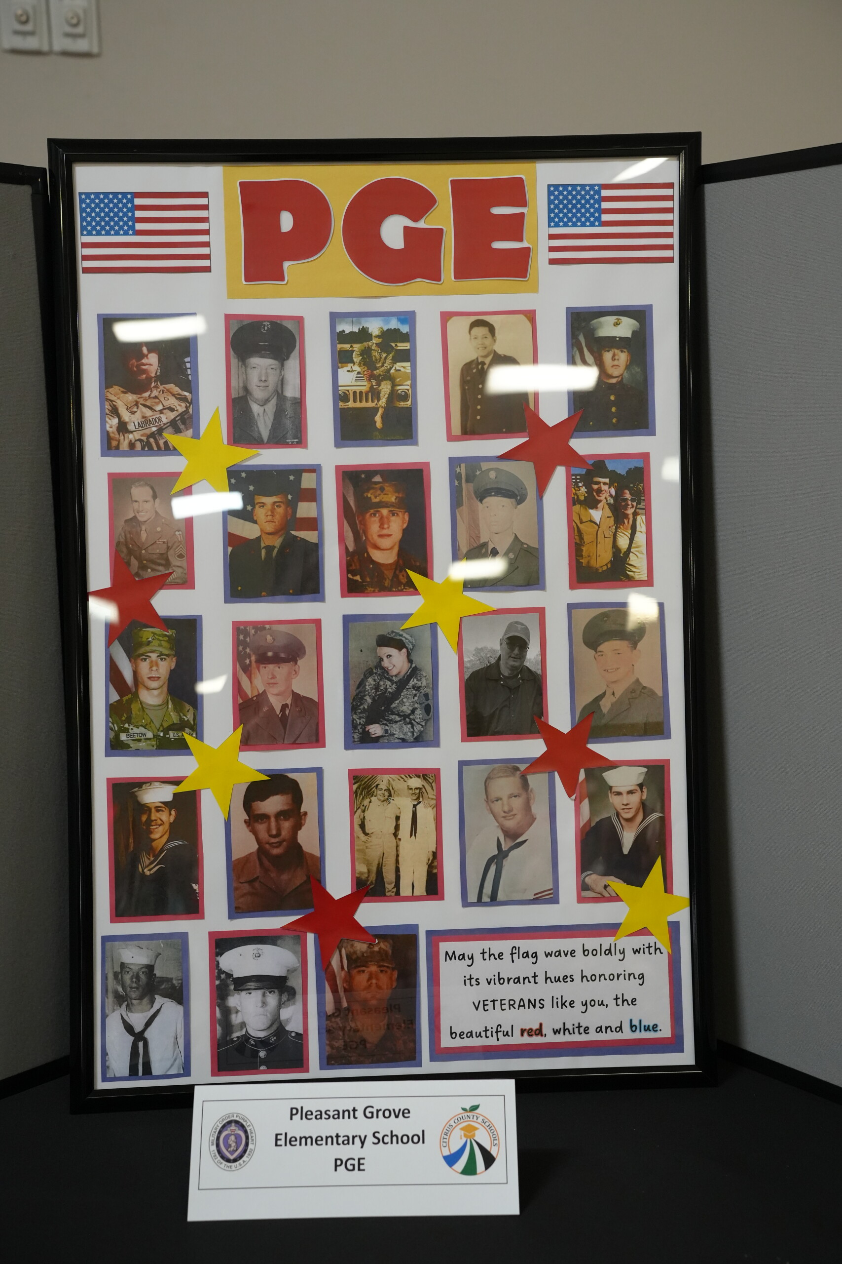 A framed collage display from Pleasant Grove Elementary honoring veterans, featuring many portrait photos and American flags.